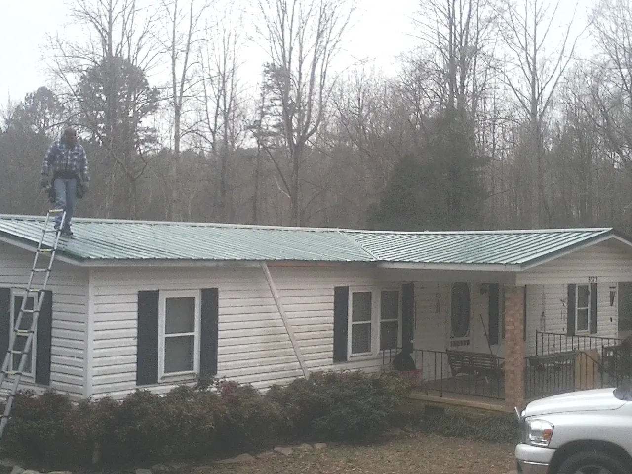 Worker on a ladder beside a new green metal roof on a ranch home in Ashland