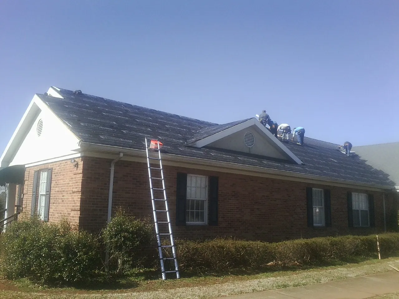 Crew tearing shingles off a brick ranch roof with a ladder set — Metal Roof Repair work by our crew in Ashland